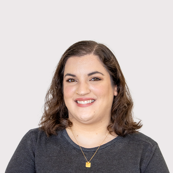 Portrait of a smiling woman with shoulder-length hair, wearing a dark sweater and a gold necklace.